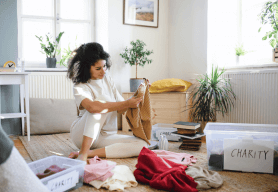 a woman sits on the floor and sorts through her belongings into boxes marked 'charity'