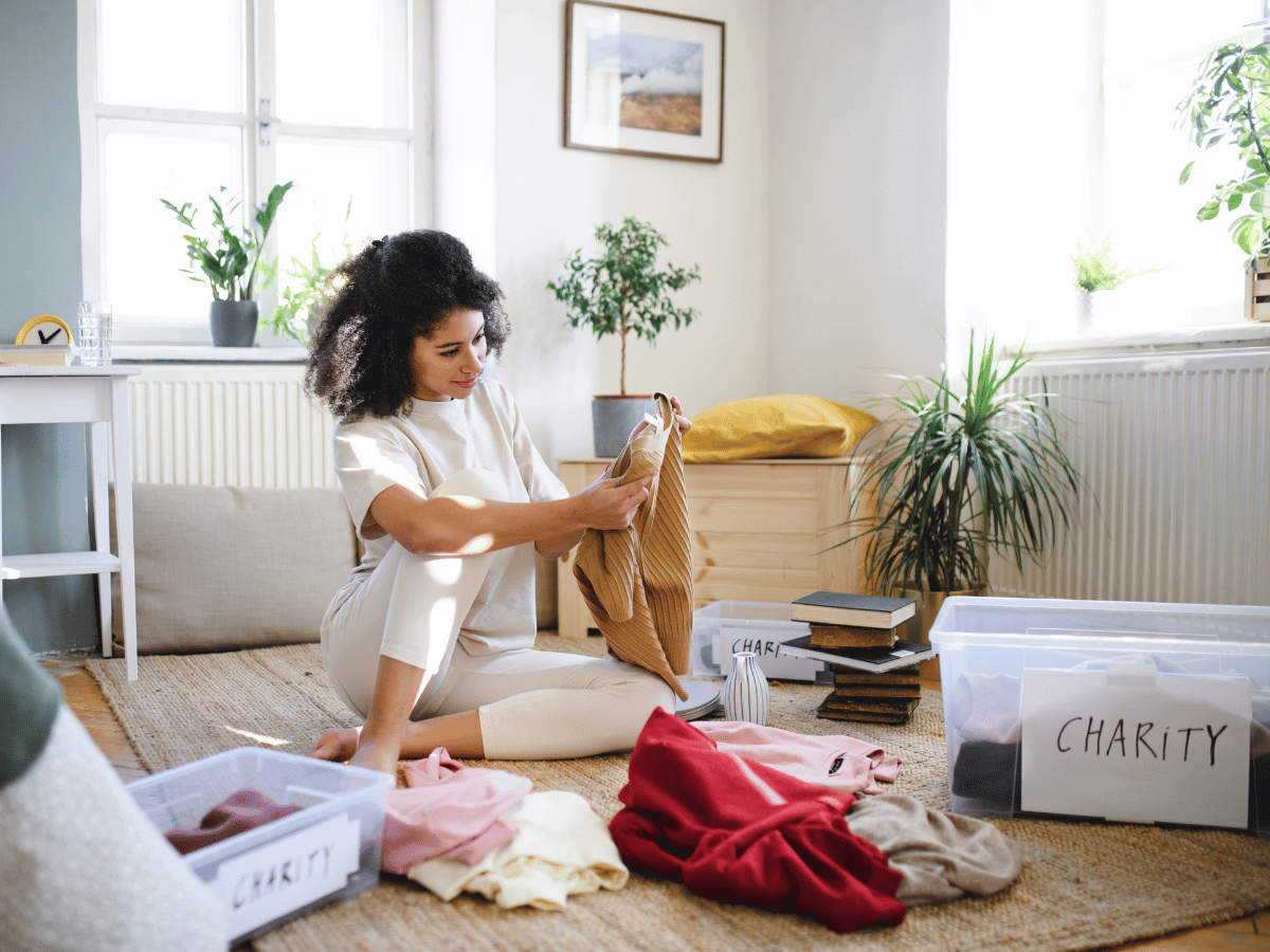 a woman sits on the floor and sorts through her belongings into boxes marked 'charity'