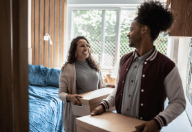 A mother helps her son to move to University. They are carrying packing boxes out of the bedroom to go into a storage unit.
