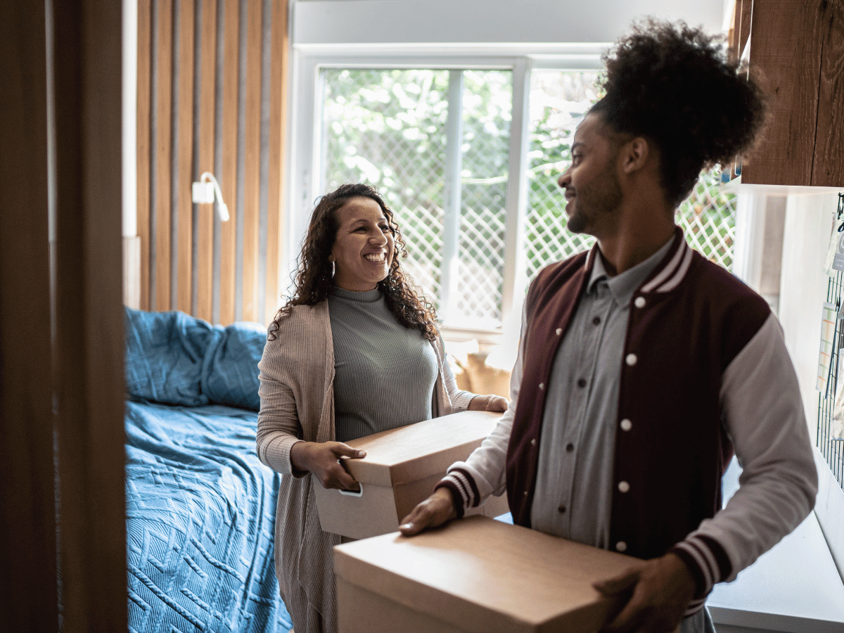 A mother helps her son to move to University. They are carrying packing boxes out of the bedroom to go into a storage unit.