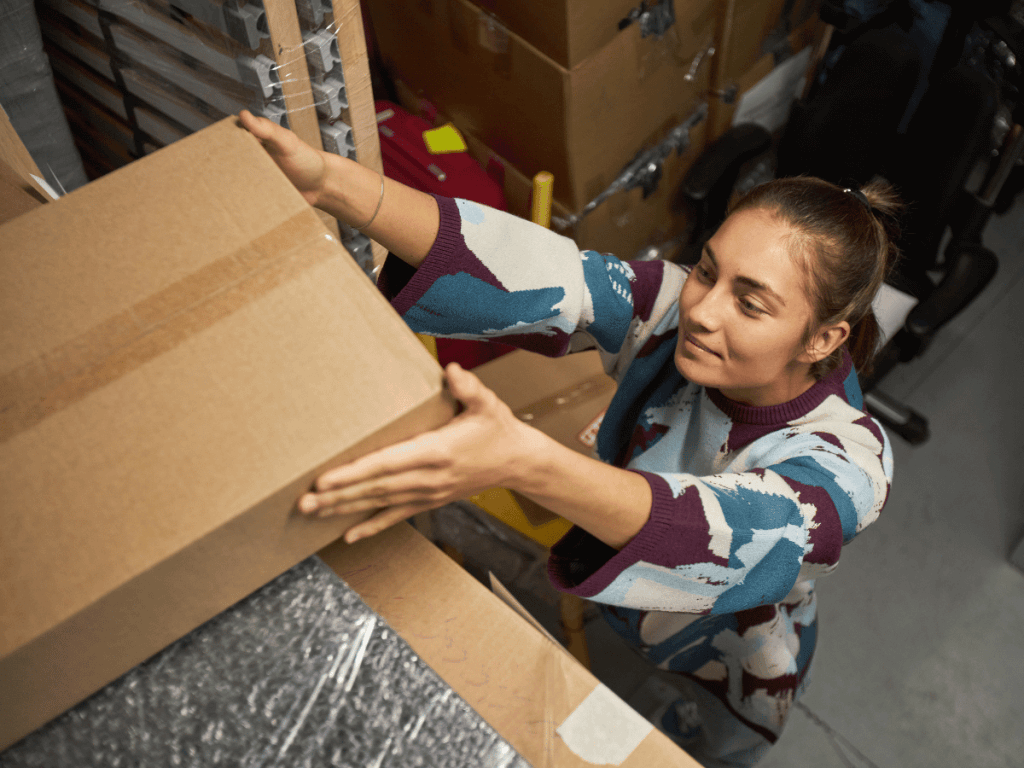 a casually dressed female small business owner puts a box on the shelf of her storage unit.